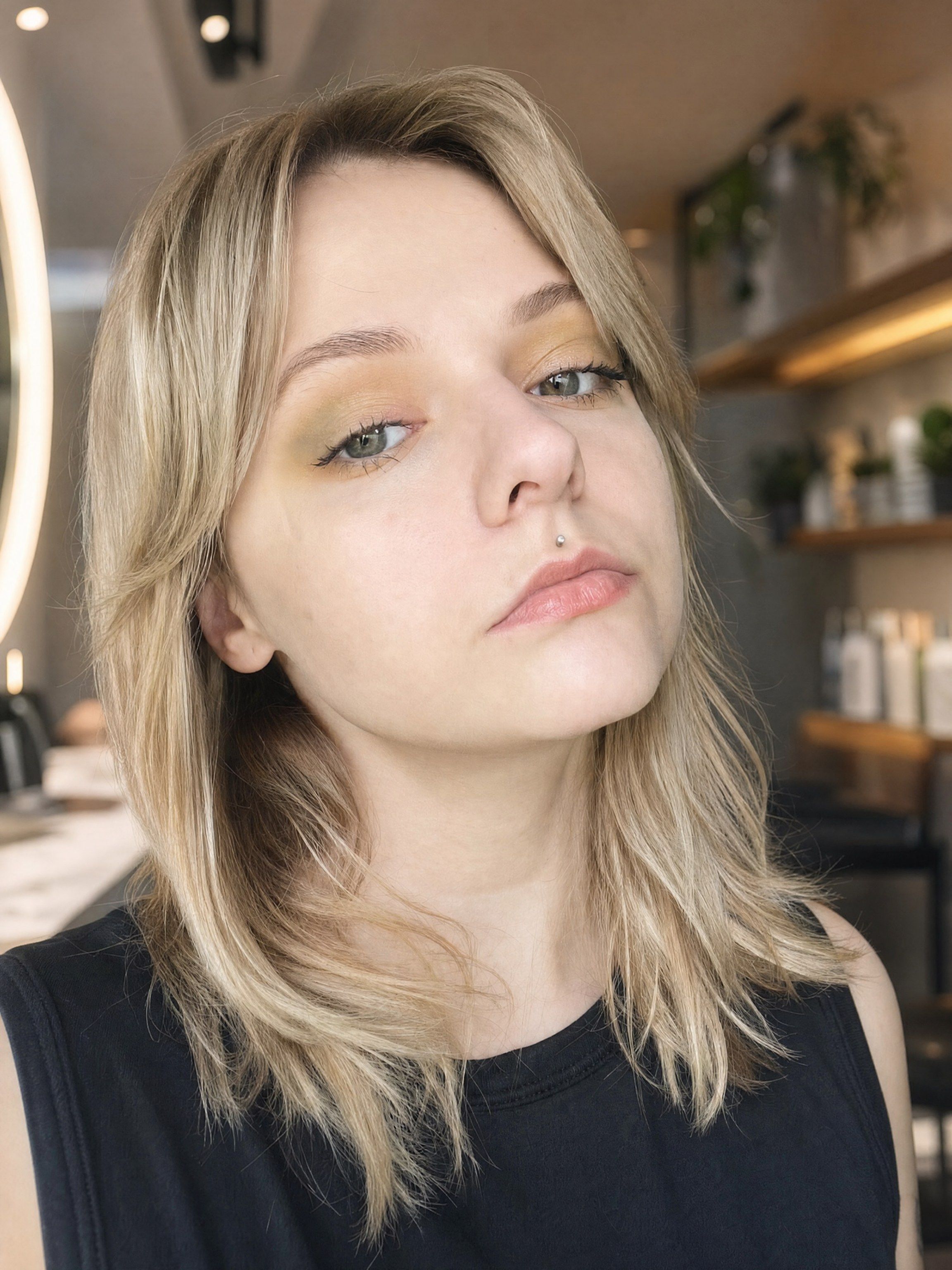 Savannah, Everfern stylist, with layered blonde hair, in the salon beside a lit ring mirror