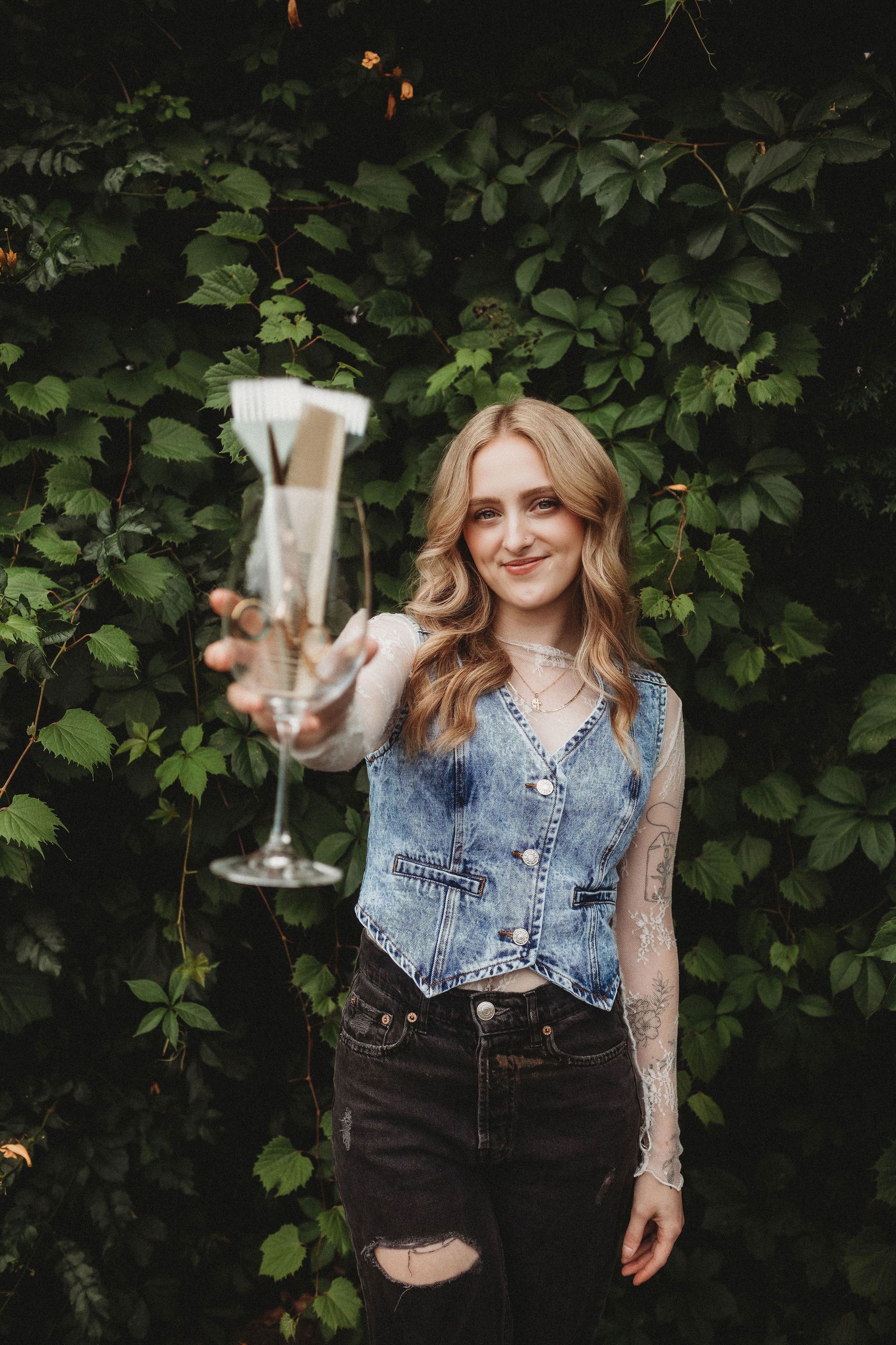 Sydnee, Everfern stylist, holding a glass of color brushes against a wall of green ivy